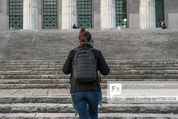 Porträt einer jungen Frau  die auf dem Rücken liegend die Treppen ihrer Universität hinaufgeht