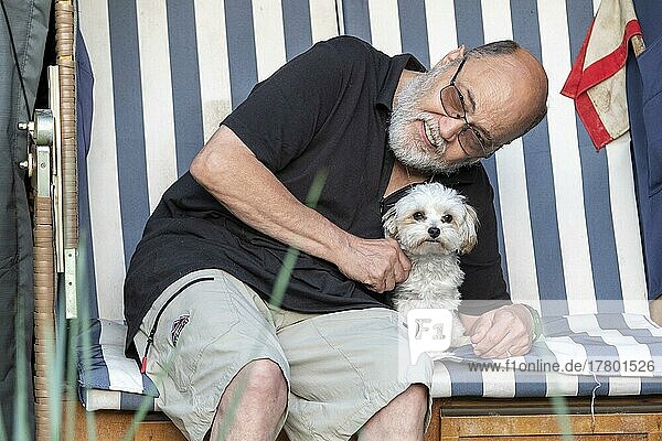 Elderly gentleman posing with Bolonka Zwetna dog in beach chair  Reppenstedt  Lower Saxony  Germany  Europe