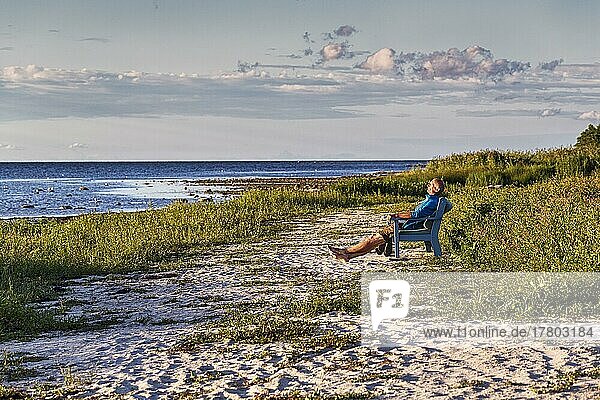 Spaziergänger genießt Abendsonne auf Bank am Naturstrand  Sandstrand  Bucht von Ekeviken  Insel Fårö  Farö  Gotland  Ostsee  Schweden  Europa