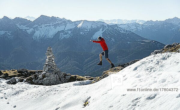 Mountaineer jumping  next to a cairn  in front of snow-covered mountains of the Rofan  hiking trail to the Guffert with first snow  in autumn  Brandenberg Alps  Tyrol  Austria  Europe