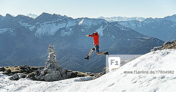 Bergsteiger im Sprung  neben einem Steinmännchen  vor verschneiten Bergen des Rofan  Wanderweg zum Guffert mit erstem Schnee  im Herbst  Brandenberger Alpen  Tirol  Österreich  Europa