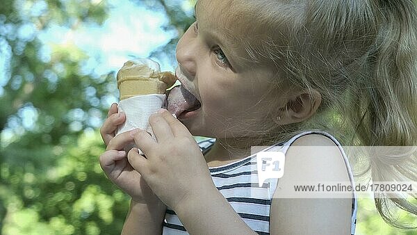 Süßes kleines Mädchen isst draußen Eis. Close-up-Porträt von blonden Mädchen sitzen auf Parkbank und essen Eis. Odessa Ukraine