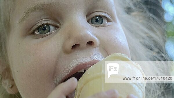 Süßes kleines Mädchen isst draußen Eis. Close-up-Porträt von blonden Mädchen sitzen auf Parkbank und essen Eis. Odessa  Ukraine  Europa