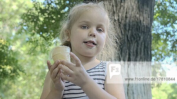 Cute little girl eats ice cream outside. Close-up portrait of blonde girl sitting on park bench and eating icecream. Odessa Ukraine