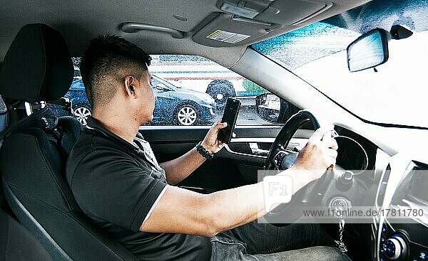 Abgelenkter Fahrer  der während der Fahrt das Handy benutzt  Mann  der während der Fahrt sein Handy benutzt  Person  die das Handy hält und mit der anderen Hand das Lenkrad  Konzept des unverantwortlichen Fahrens