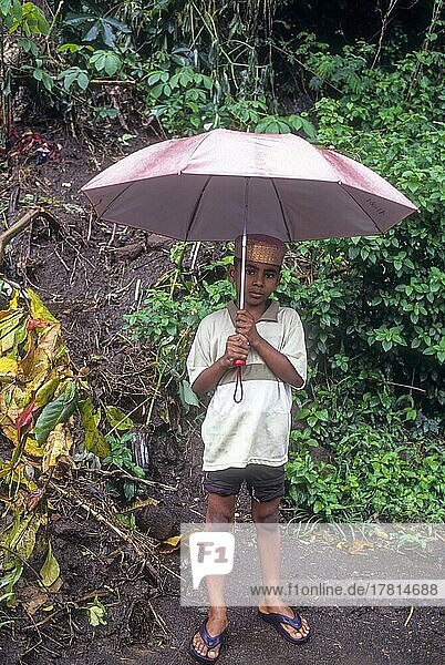 Ein Junge steht mit einem Regenschirm an einem regnerischen Tag in Attappadi  Kerala  Indien  Asien