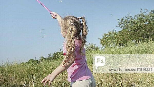 Kleines Mädchen fängt Seifenblasen in Schmetterlingsnetz beim Spielen im hohen Gras im Park. Nettes kleines Mädchen lächelt und fängt auf Seifenblasen in Antenne Insektennetz in Wiese auf Sonne Tag. Odessa  Ukraine  Europa
