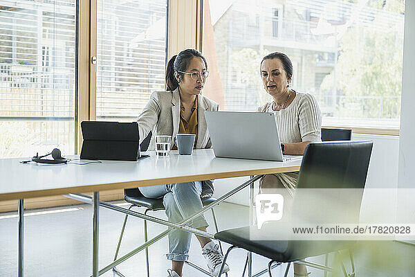 Mature businesswoman with colleague discussing over laptop in office