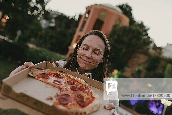Frau mit geschlossenen Augen zeigt Pizza im Karton