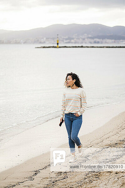 Reife Frau mit Handy geht am Strand spazieren