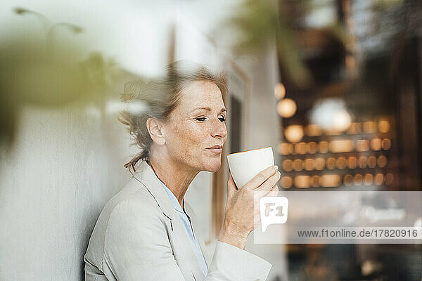 Businesswoman having coffee in cafe seen through glass