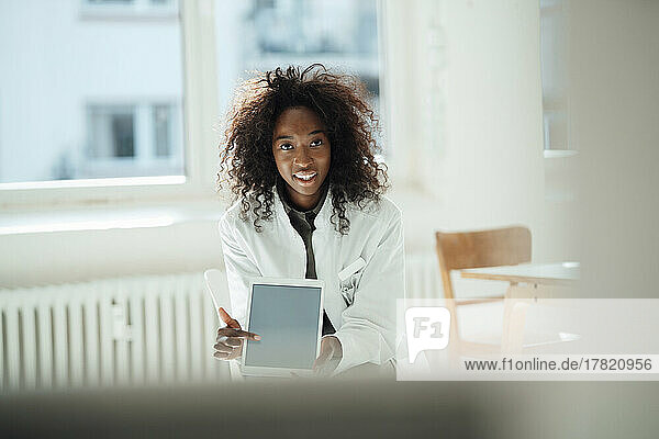 Smiling female doctor with curly hair pointing at tablet PC