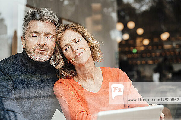 Smiling couple with eyes closed sitting in cafe seen through glass