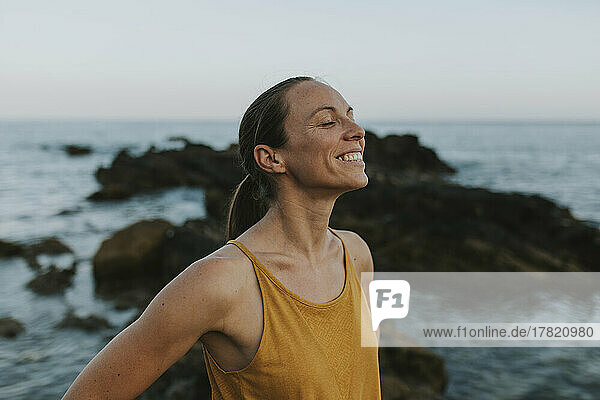 Lächelnde Frau mit geschlossenen Augen  die am Meeresufer genießt