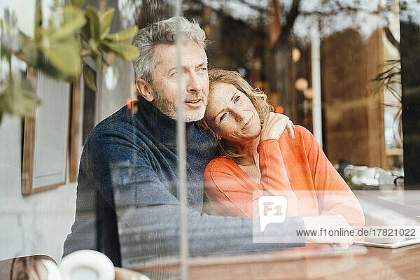 Man embracing woman sitting in cafe seen through glass