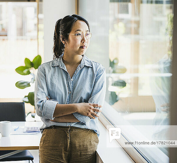 Contemplative businesswoman with arms crossed by window