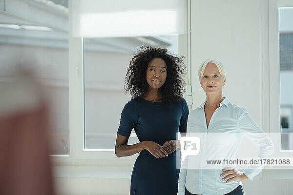 Smiling businesswoman with hand on hip standing by colleague in office