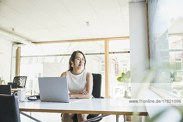 Lächelnde Geschäftsfrau mit Laptop auf dem Schreibtisch im Büro