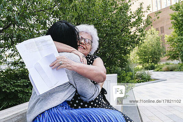 Ältere Mutter umarmt liebevoll Tochter  die im Park sitzt