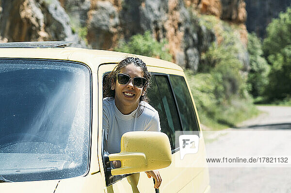 Happy woman looking through van window on sunny day