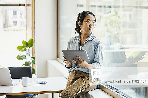 Businesswoman with tablet PC looking through window