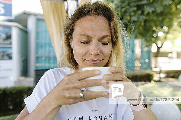 Lächelnde Frau mit geschlossenen Augen und Kaffeetasse im Resort
