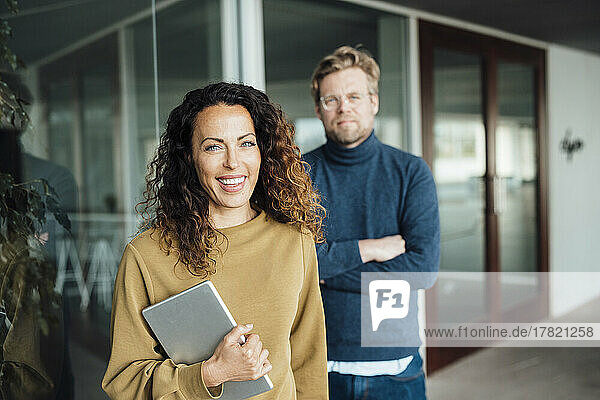 Smiling businesswoman holding digital tablet standing with colleague at office