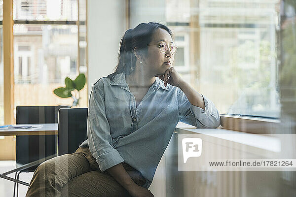 Businesswoman with hand on chin seen through glass of office