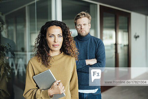 Confident businesswoman holding digital tablet standing with colleague