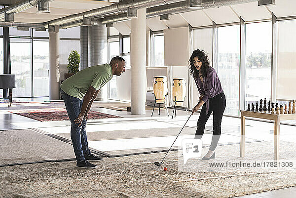 Happy businesswoman playing golf in office