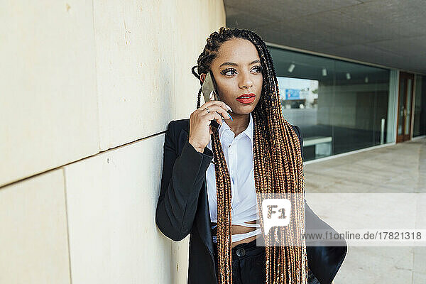 Young businesswoman talking through smart phone leaning on wall