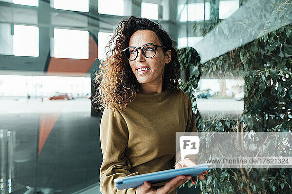 Lächelnde Geschäftsfrau mit Tablet-PC steht am Arbeitsplatz