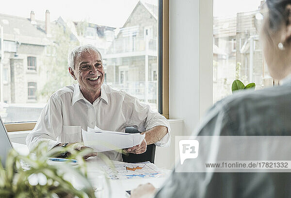 Happy businessman with documents by colleague in office