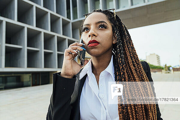 Junge Geschäftsfrau spricht mit Smartphone vor Bürogebäude