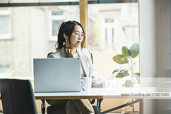 Businesswoman with eyeglasses reading document at desk