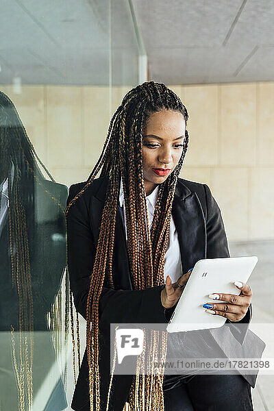 Young businesswoman with tablet PC leaning on glass wall