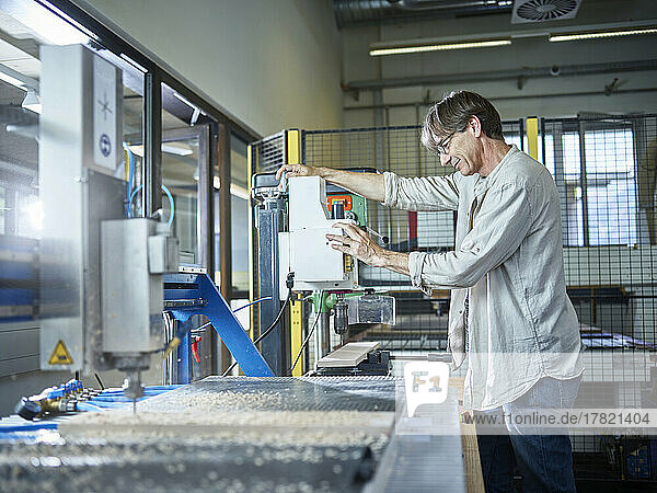Mature man working on wood machine in factory