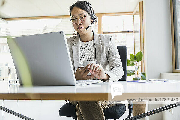 Smiling businesswoman with headset working on laptop at desk