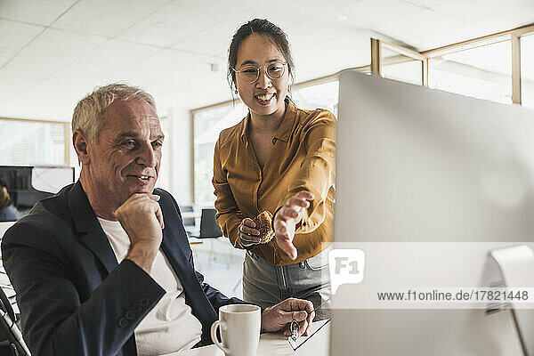 Happy businesswoman with colleague discussing over desktop PC in office