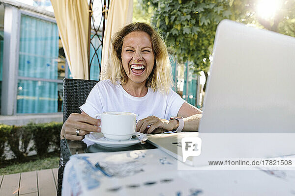 Cheerful woman with coffee cup sitting at table