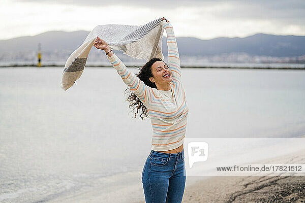 Fröhliche Frau mit erhobenen Armen und Schal am Strand