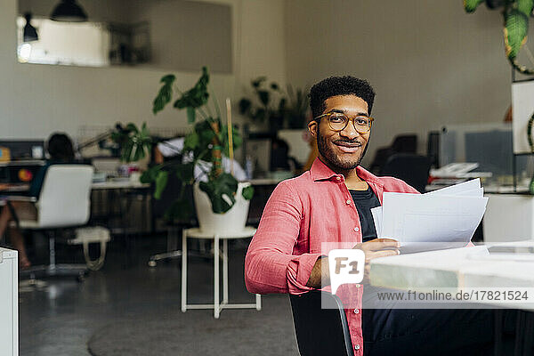 Smiling businessman with documents at desk at office