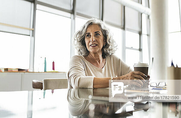 Senior businesswoman with coffee cup sitting at desk