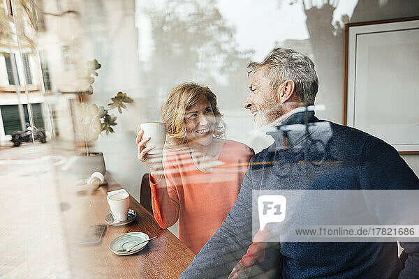 Happy man talking with woman holding coffee cup in cafe