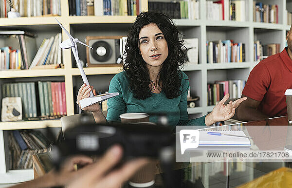 Businesswoman holding wind turbine model talking to colleagues in office