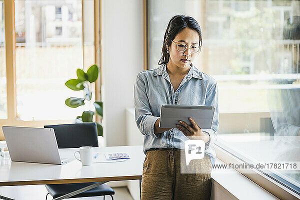 Businesswoman using tablet PC standing by window in office
