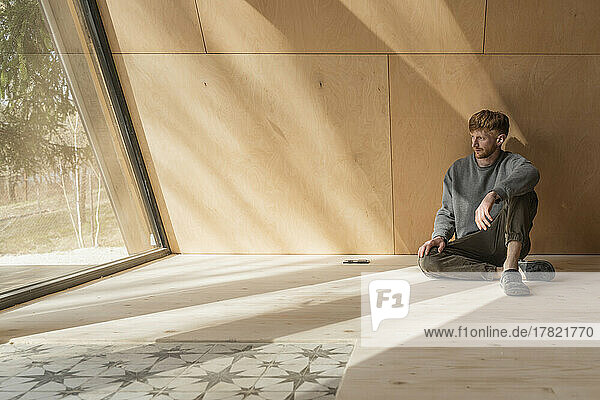 Mann sitzt auf dem Boden in einem Öko-Holzhaus und schaut aus dem Fenster