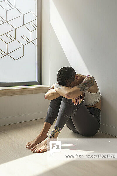 Sad tattooed woman sitting by window at home