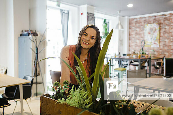 Glückliche Geschäftsfrau  gesehen durch Pflanzen im Büro