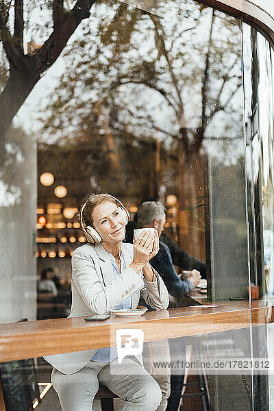 Businesswoman holding coffee cup enjoying music listening through wireless headphones in cafe